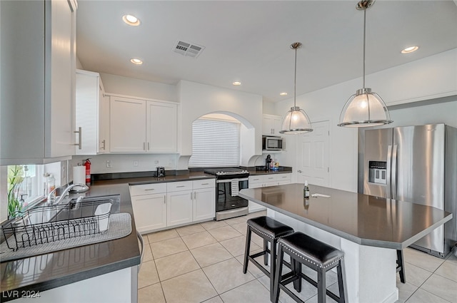 kitchen with stainless steel appliances, a breakfast bar, a center island, decorative light fixtures, and white cabinetry