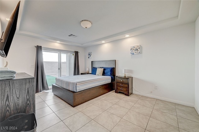 bedroom with a tray ceiling, light tile patterned floors, and access to exterior