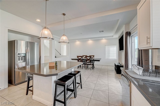 kitchen with light tile patterned floors, white cabinetry, a kitchen bar, decorative light fixtures, and stainless steel appliances