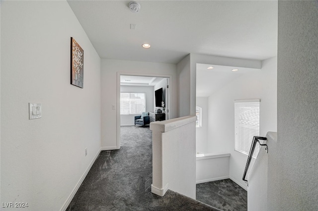 hall featuring lofted ceiling and dark colored carpet