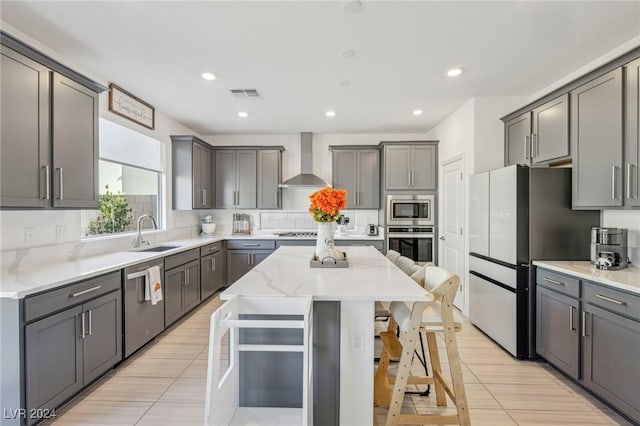 kitchen with sink, appliances with stainless steel finishes, a kitchen breakfast bar, a center island, and wall chimney exhaust hood