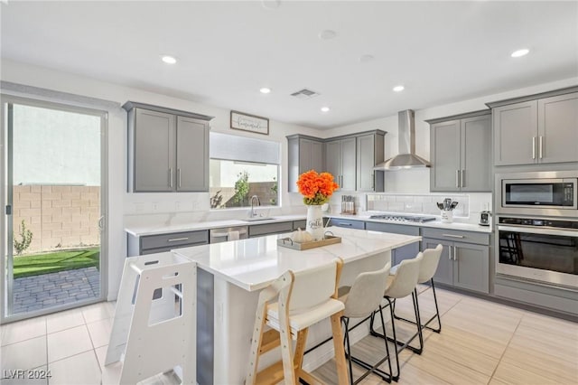 kitchen featuring a breakfast bar, sink, gray cabinetry, appliances with stainless steel finishes, and wall chimney range hood