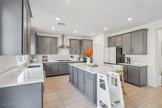 kitchen featuring gray cabinets, a center island, sink, and wall chimney range hood