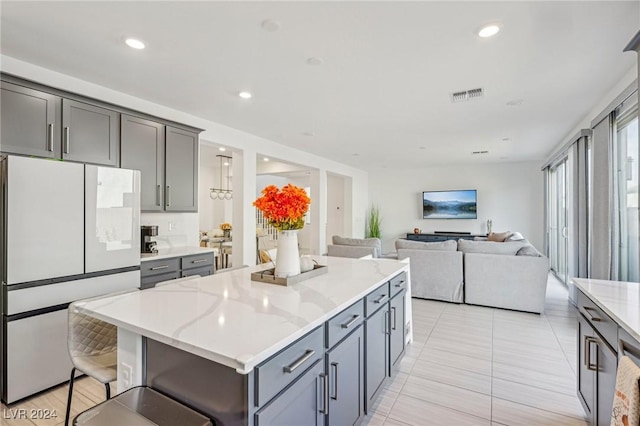 kitchen featuring gray cabinets, a kitchen island, a kitchen bar, white refrigerator, and light stone countertops