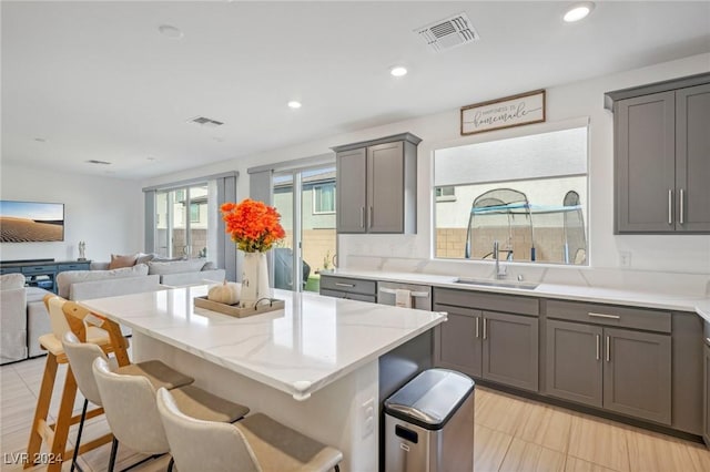 kitchen with sink, a breakfast bar area, dishwasher, gray cabinetry, and a center island