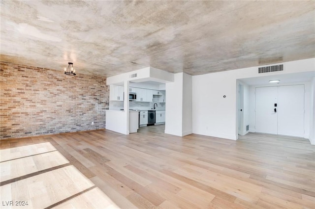 unfurnished living room with sink, light hardwood / wood-style flooring, and brick wall