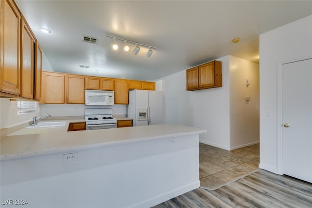 kitchen featuring kitchen peninsula, white appliances, sink, rail lighting, and light hardwood / wood-style floors