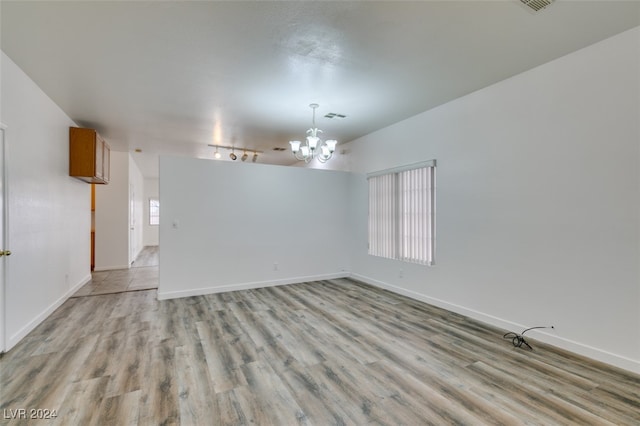 spare room featuring a notable chandelier and light wood-type flooring