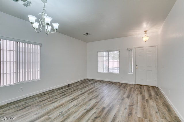 unfurnished room with a notable chandelier and light wood-type flooring