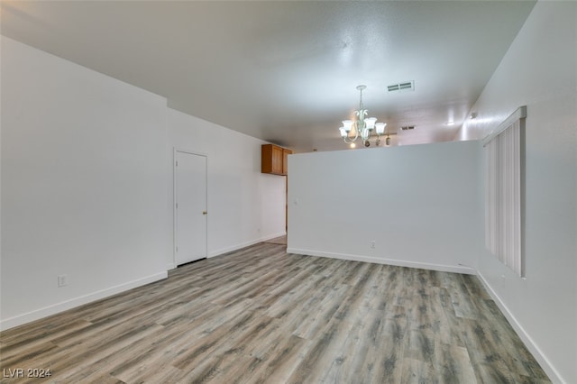 spare room featuring a notable chandelier and light wood-type flooring