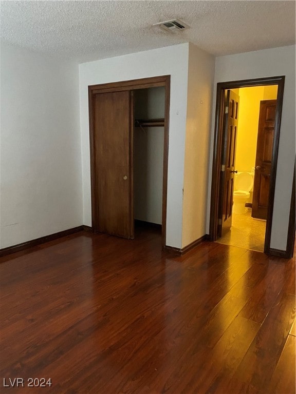 unfurnished bedroom featuring a closet, a textured ceiling, and dark hardwood / wood-style flooring