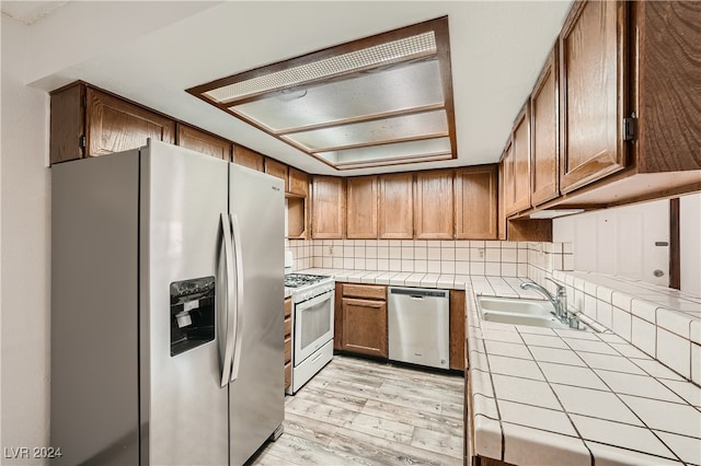 kitchen with light hardwood / wood-style flooring, tile countertops, appliances with stainless steel finishes, and sink