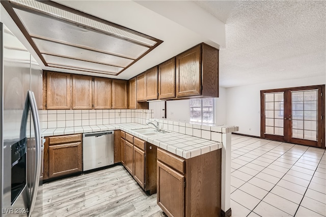 kitchen featuring sink, backsplash, kitchen peninsula, stainless steel appliances, and light tile patterned floors