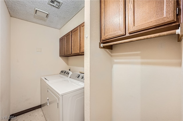 laundry area with cabinets, a textured ceiling, and washing machine and dryer