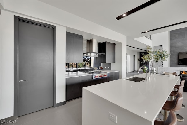 kitchen with stainless steel gas cooktop, sink, a kitchen breakfast bar, wall chimney exhaust hood, and light tile patterned floors