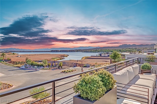 balcony at dusk featuring a water and mountain view