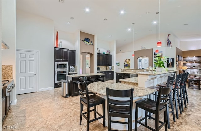 kitchen featuring light stone counters, a large island, a kitchen breakfast bar, high vaulted ceiling, and appliances with stainless steel finishes