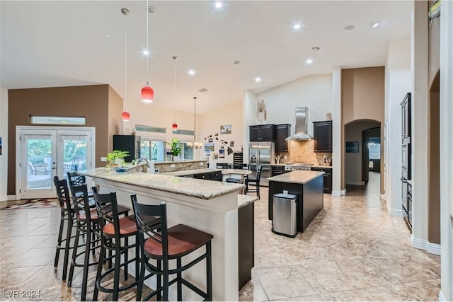 kitchen with wall chimney exhaust hood, a large island, a breakfast bar, light stone countertops, and pendant lighting