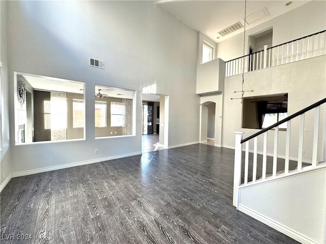 unfurnished living room featuring a wealth of natural light, dark hardwood / wood-style flooring, ceiling fan, and a high ceiling