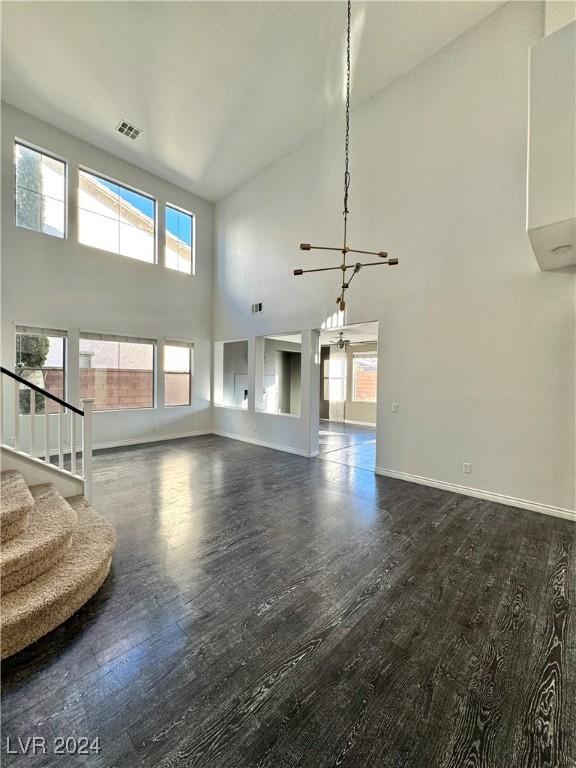 unfurnished living room featuring a towering ceiling, a chandelier, and dark hardwood / wood-style floors