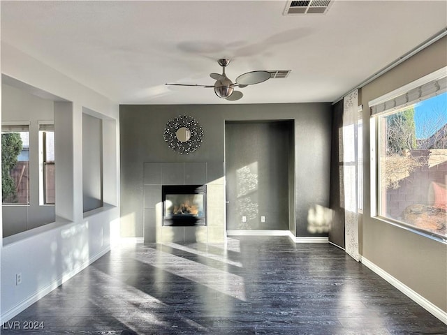 unfurnished living room with ceiling fan, dark hardwood / wood-style flooring, a wealth of natural light, and a tiled fireplace