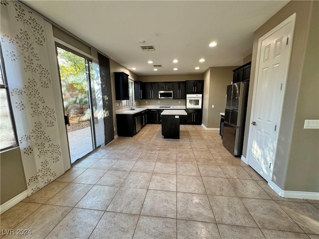 kitchen with light tile patterned floors, stainless steel appliances, a kitchen island, and sink