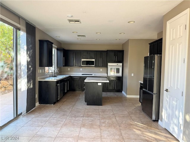 kitchen with light tile patterned floors, stainless steel appliances, a kitchen island, and sink