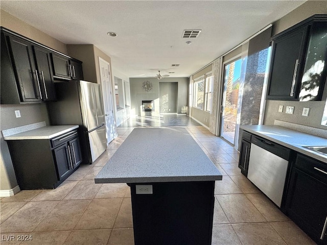 kitchen featuring a kitchen island, light tile patterned floors, appliances with stainless steel finishes, and a tiled fireplace