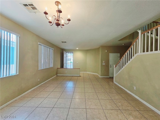 spare room featuring light tile patterned flooring, a textured ceiling, and a notable chandelier