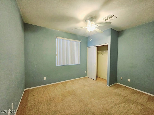 unfurnished bedroom featuring a closet, a textured ceiling, light carpet, and ceiling fan