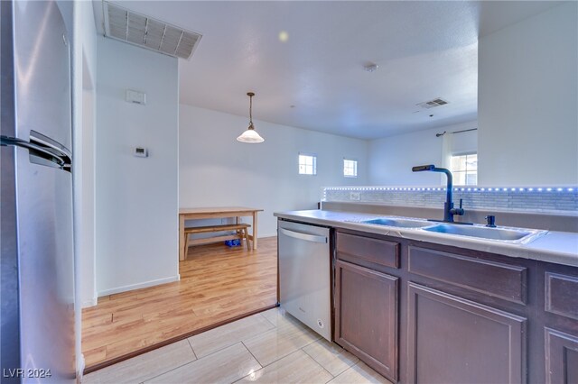 kitchen with sink, hanging light fixtures, decorative backsplash, light wood-type flooring, and stainless steel appliances