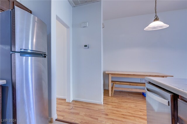 kitchen with decorative light fixtures, stainless steel appliances, and light hardwood / wood-style flooring