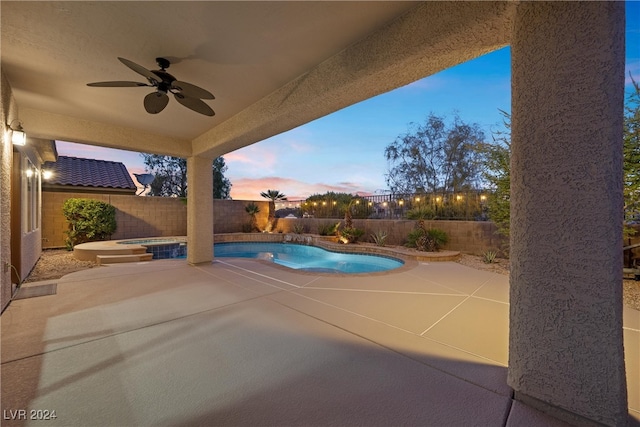 pool at dusk with ceiling fan and a patio