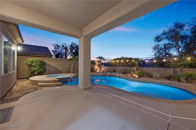 pool at dusk with an in ground hot tub and a patio area