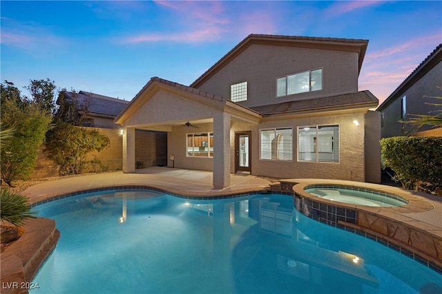 pool at dusk featuring a patio area, ceiling fan, and an in ground hot tub