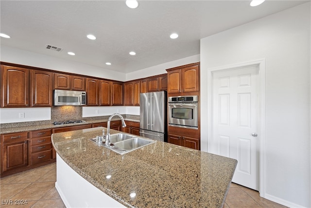 kitchen featuring stainless steel appliances, light tile patterned floors, sink, and an island with sink