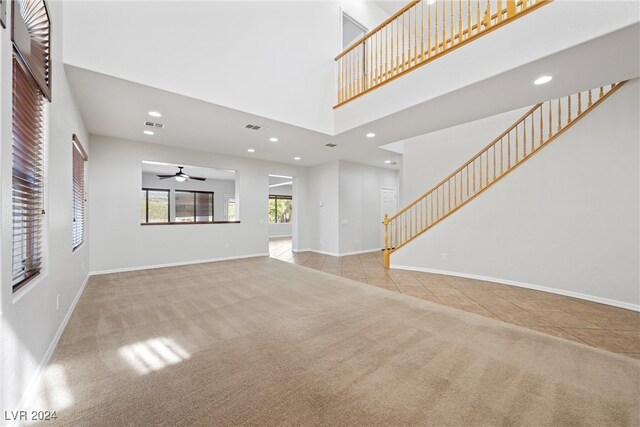 unfurnished living room with ceiling fan, a high ceiling, and light colored carpet