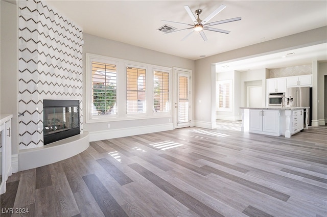 unfurnished living room featuring a fireplace, ceiling fan, and light hardwood / wood-style flooring