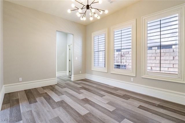 spare room with light wood-type flooring, a wealth of natural light, and an inviting chandelier