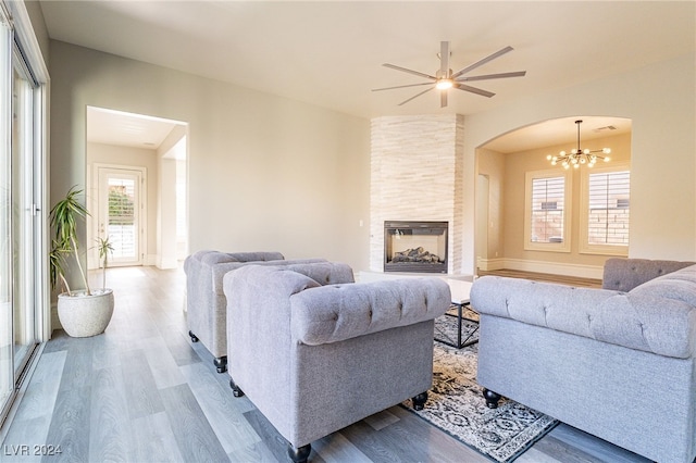 living room with a fireplace, a wealth of natural light, light hardwood / wood-style floors, and ceiling fan with notable chandelier