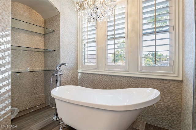 bathroom with tile walls, a washtub, wood-type flooring, and an inviting chandelier