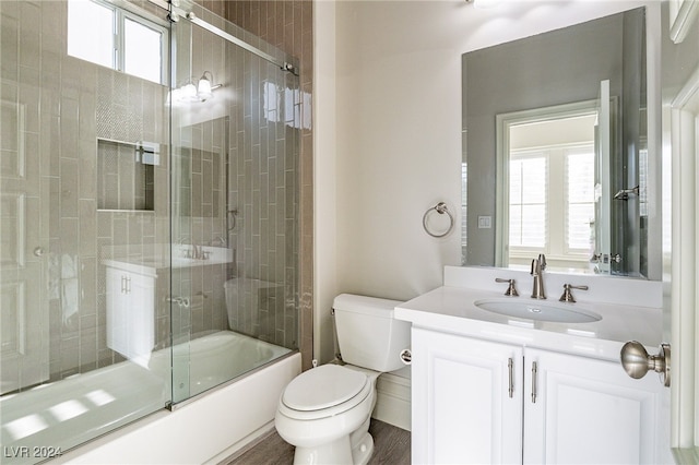 full bathroom featuring hardwood / wood-style floors, vanity, combined bath / shower with glass door, and toilet