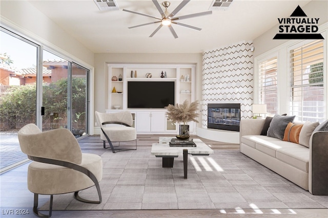 living room with a fireplace, a wealth of natural light, built in features, and ceiling fan