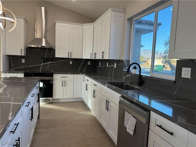 kitchen featuring pendant lighting, wall chimney range hood, white cabinets, appliances with stainless steel finishes, and sink