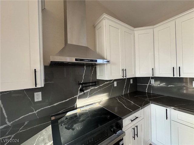 kitchen featuring white cabinets, dark stone countertops, decorative backsplash, range, and wall chimney range hood