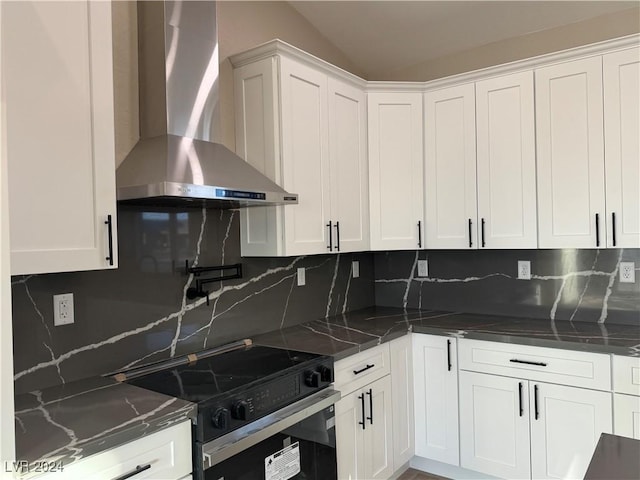 kitchen featuring dark stone countertops, stainless steel electric range, white cabinets, wall chimney range hood, and backsplash