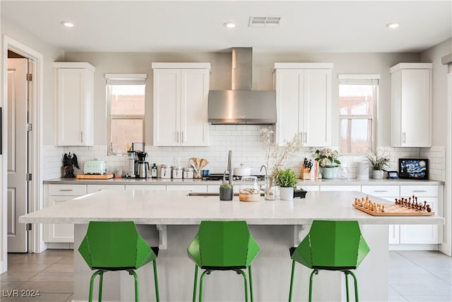 kitchen featuring white cabinetry, wall chimney range hood, and an island with sink