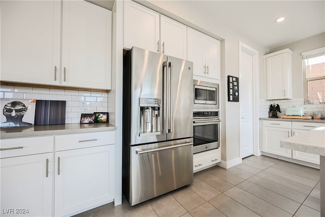 kitchen featuring tasteful backsplash, white cabinets, light tile patterned floors, and stainless steel appliances