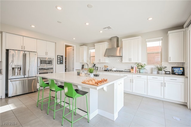 kitchen with white cabinetry, wall chimney range hood, appliances with stainless steel finishes, a kitchen breakfast bar, and a kitchen island with sink