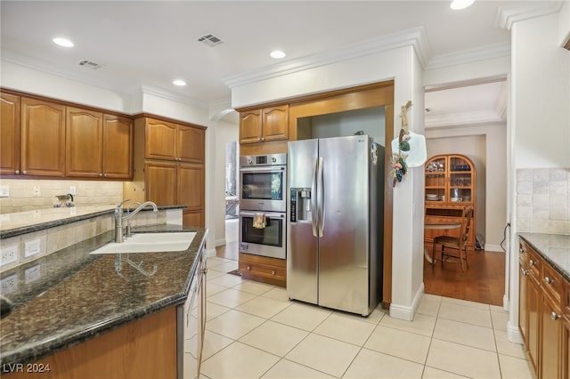 kitchen with decorative backsplash, stainless steel appliances, dark stone countertops, sink, and light tile patterned floors